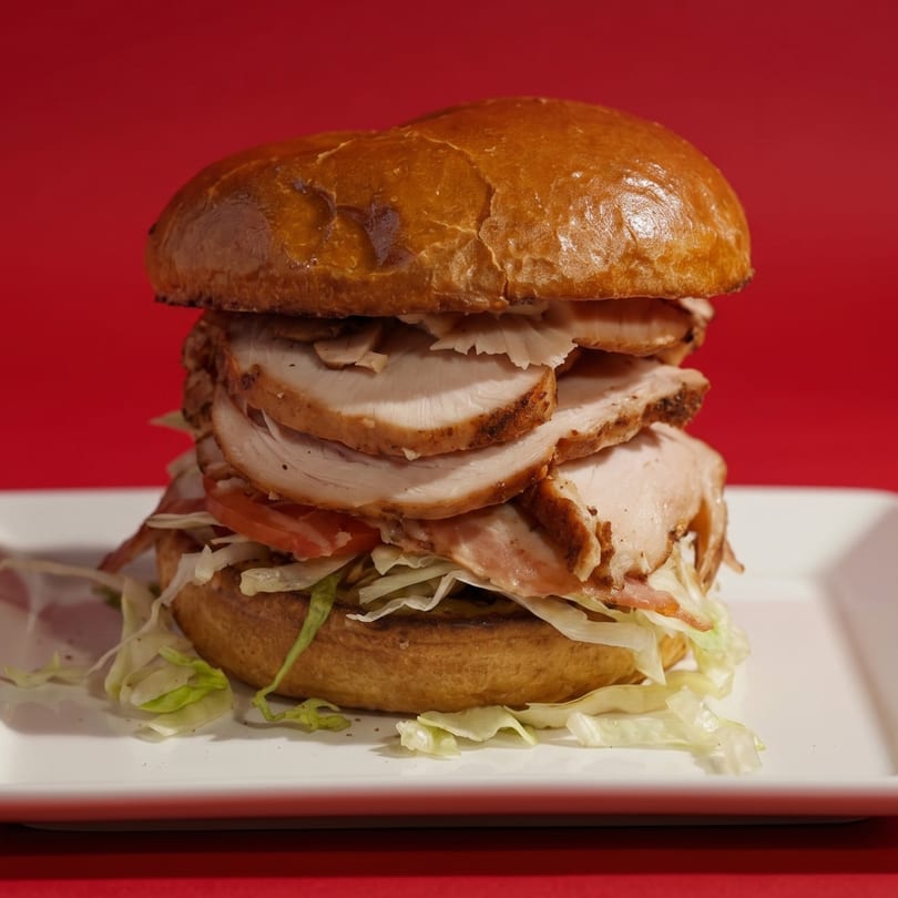 A large turkey sandwich with lettuce and tomato on a brioche bun, on a white plate.